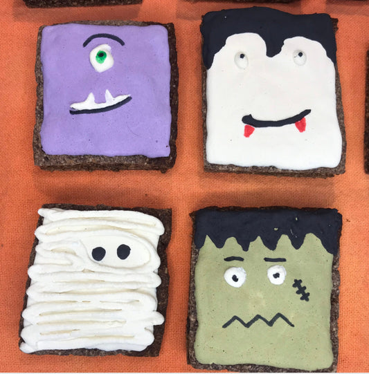 Four Halloween-themed cookies with faces on an orange background
