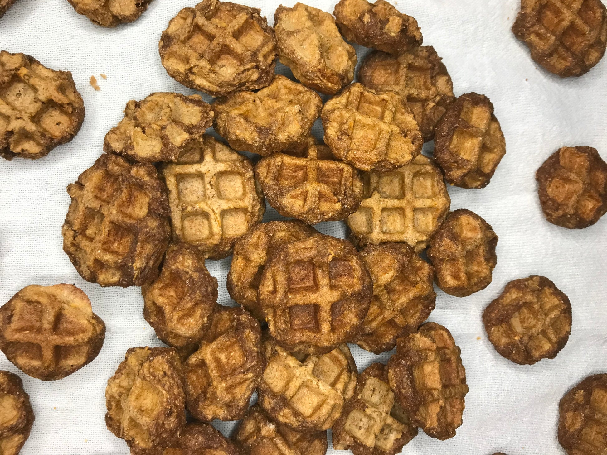 Sweet potato waffle bite dog treats. A mound of small, circular golden brown dog treats. Each treat is shaped as a bite of a waffle. Treats are appropriately 1 in x 1 in in size, approximately 8 ounces in each bag.