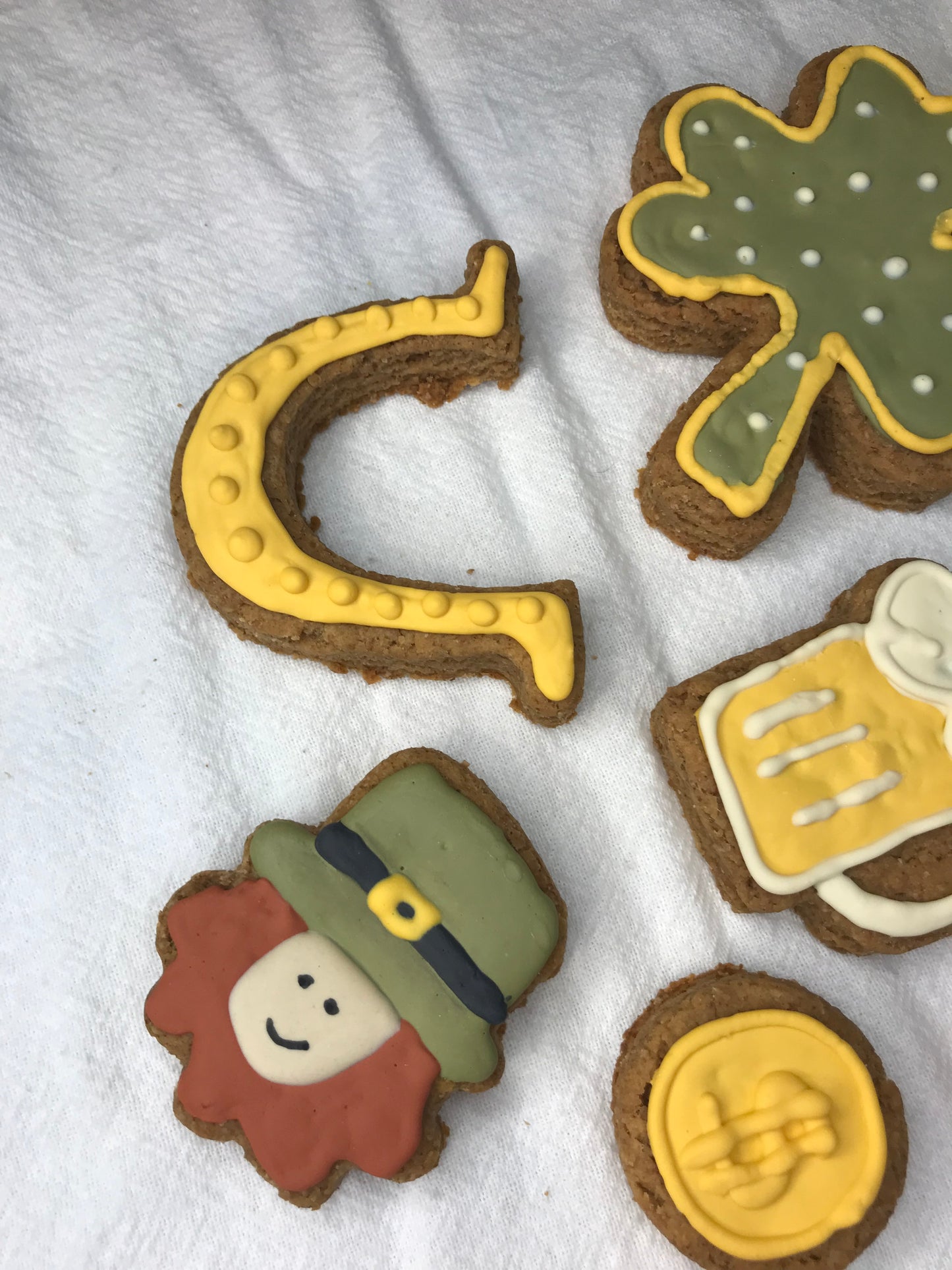 Decorative cookies shaped like a clover, beer mug, dollar sign, horseshoe, and person with a hat on a white surface.