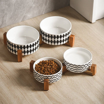 Set of four ceramic pet bowls with black geometric patterns on a wooden stand.