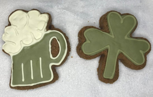Two cookies shaped like a mug and a clover with green icing on a white surface.