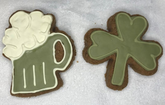 Two cookies shaped like a mug and a clover with green icing on a white surface.