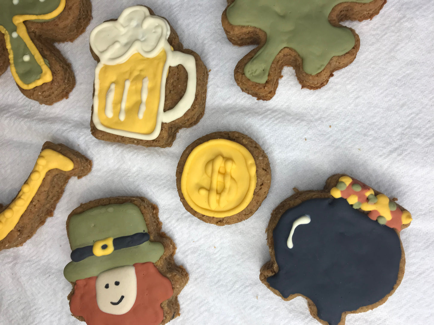 Decorative cookies shaped like a beer mug, dollar sign, leprechaun, and other designs on a white surface.