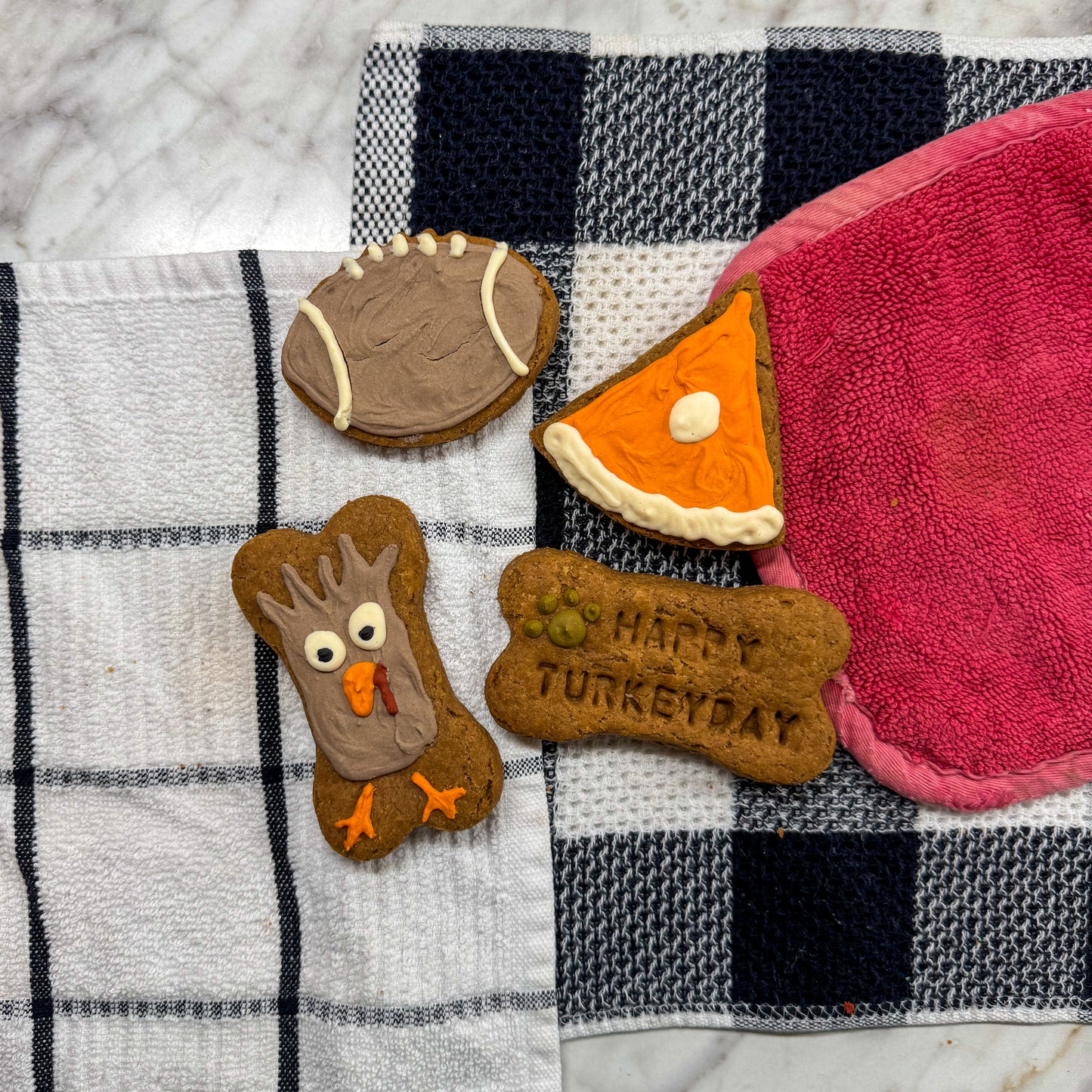 Assortment of Thanksgiving-themed dog treats, including a bone-shaped treat with a turkey face, a slice of pumpkin pie, a football, and a bone with ‘Happy Turkey Day’ stamped on it.