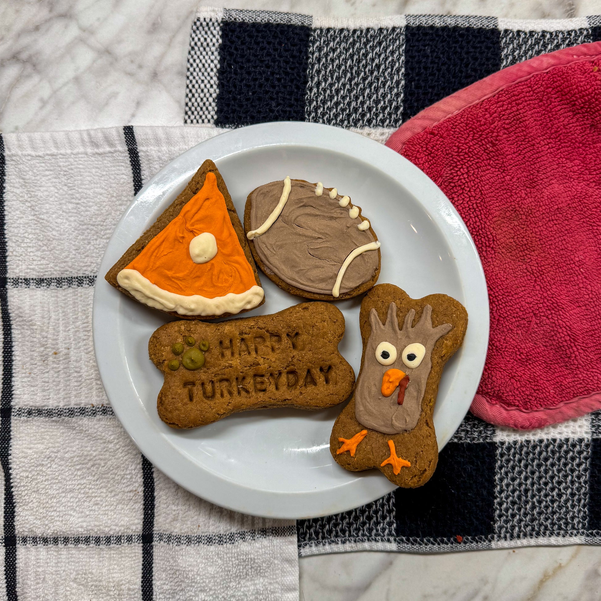 Assortment of Thanksgiving-themed dog treats, including a bone-shaped treat with a turkey face, a slice of pumpkin pie, a football, and a bone with ‘Happy Turkey Day’ stamped on it.