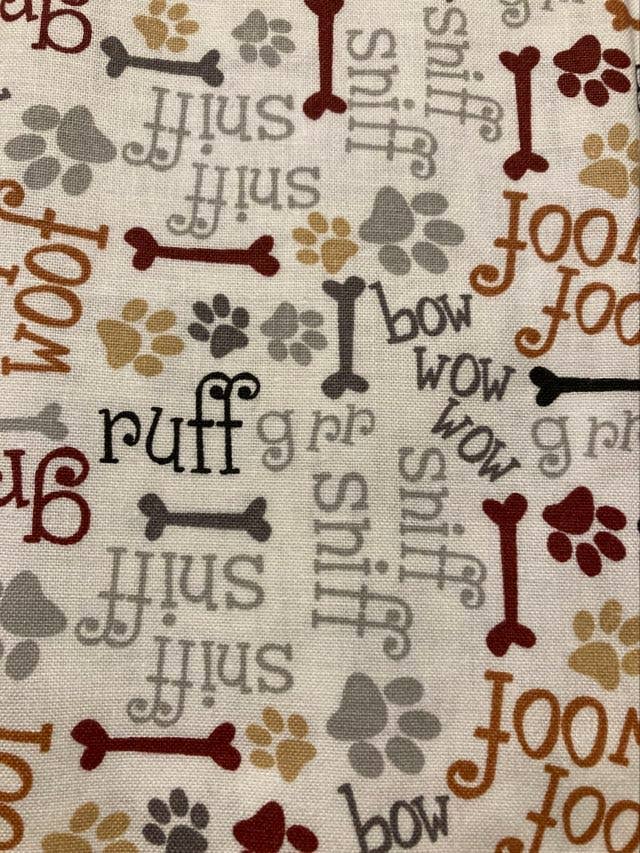 Fabric with dog-themed patterns including bones, paw prints, and text on a beige background