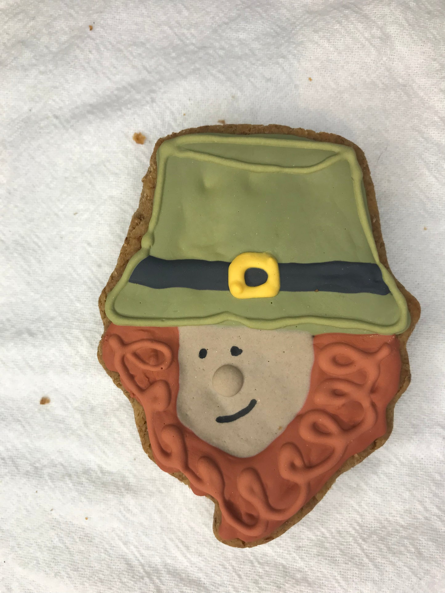 A homemade, peanut butter flavored dog treat decorated to look like a leprechaun in a hat, with a predominantly green and brown color scheme.